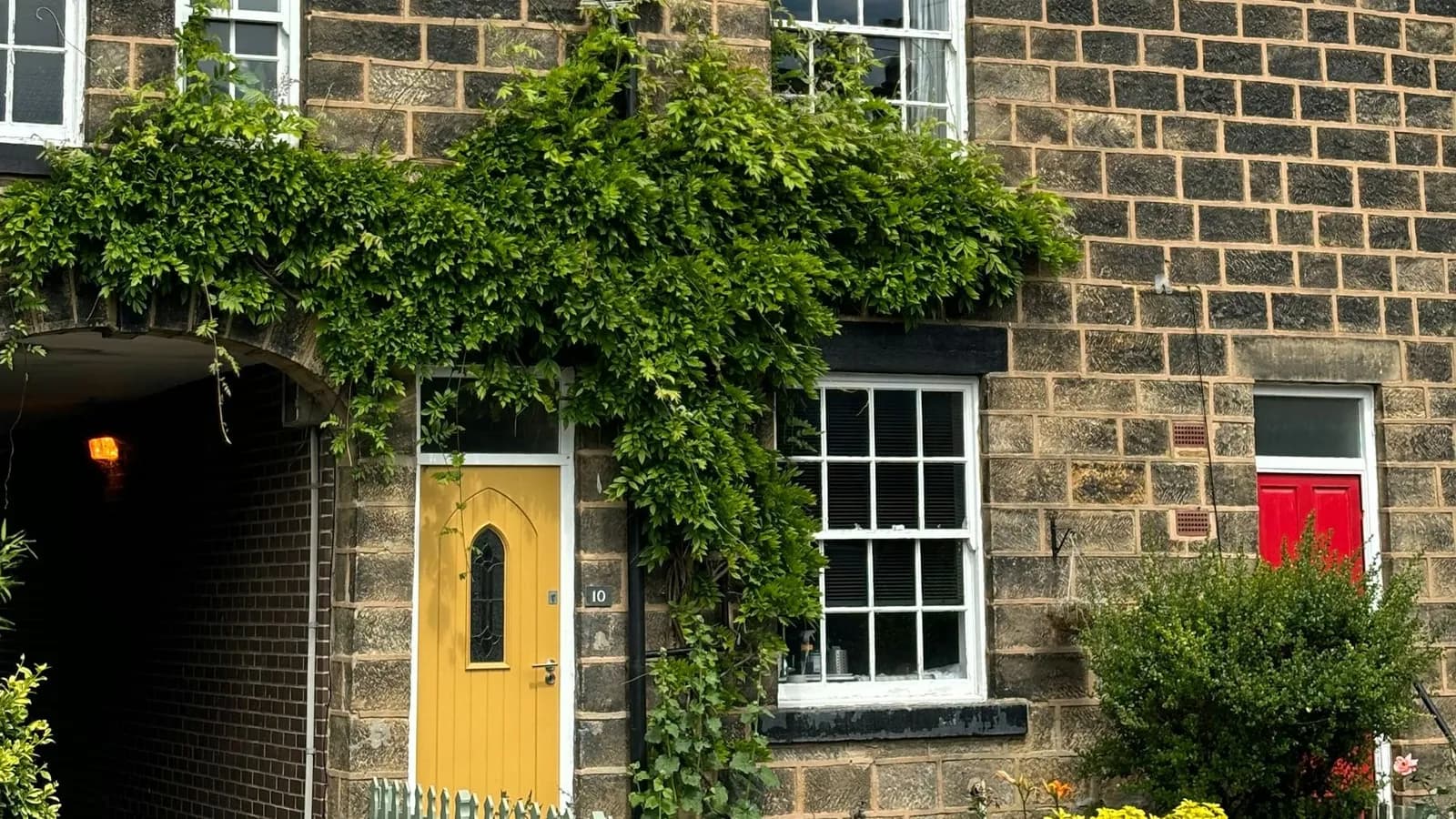 Stone-fronted terraced house with a yellow front door, sash windows and wisteria climbing the wall