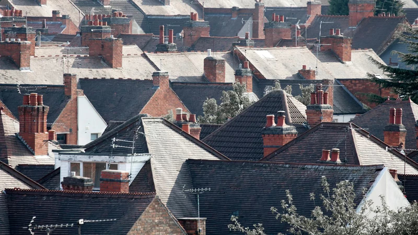 Dense rooftops of terraced houses with red chimney pots and a flat-roofed dormer on one slope