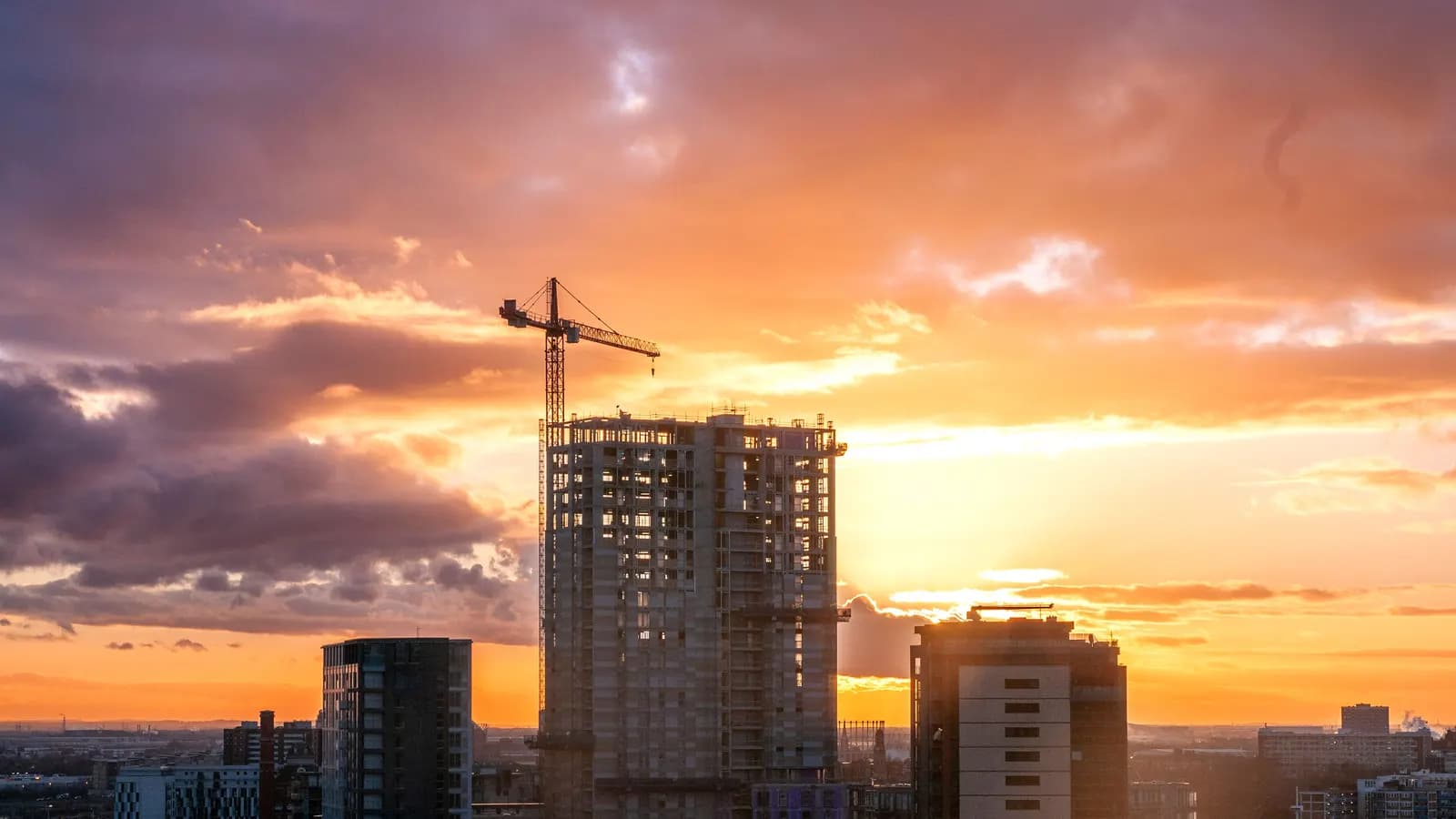 Construction site in Manchester at sunset with cranes and partly built structures against a dramatic sky