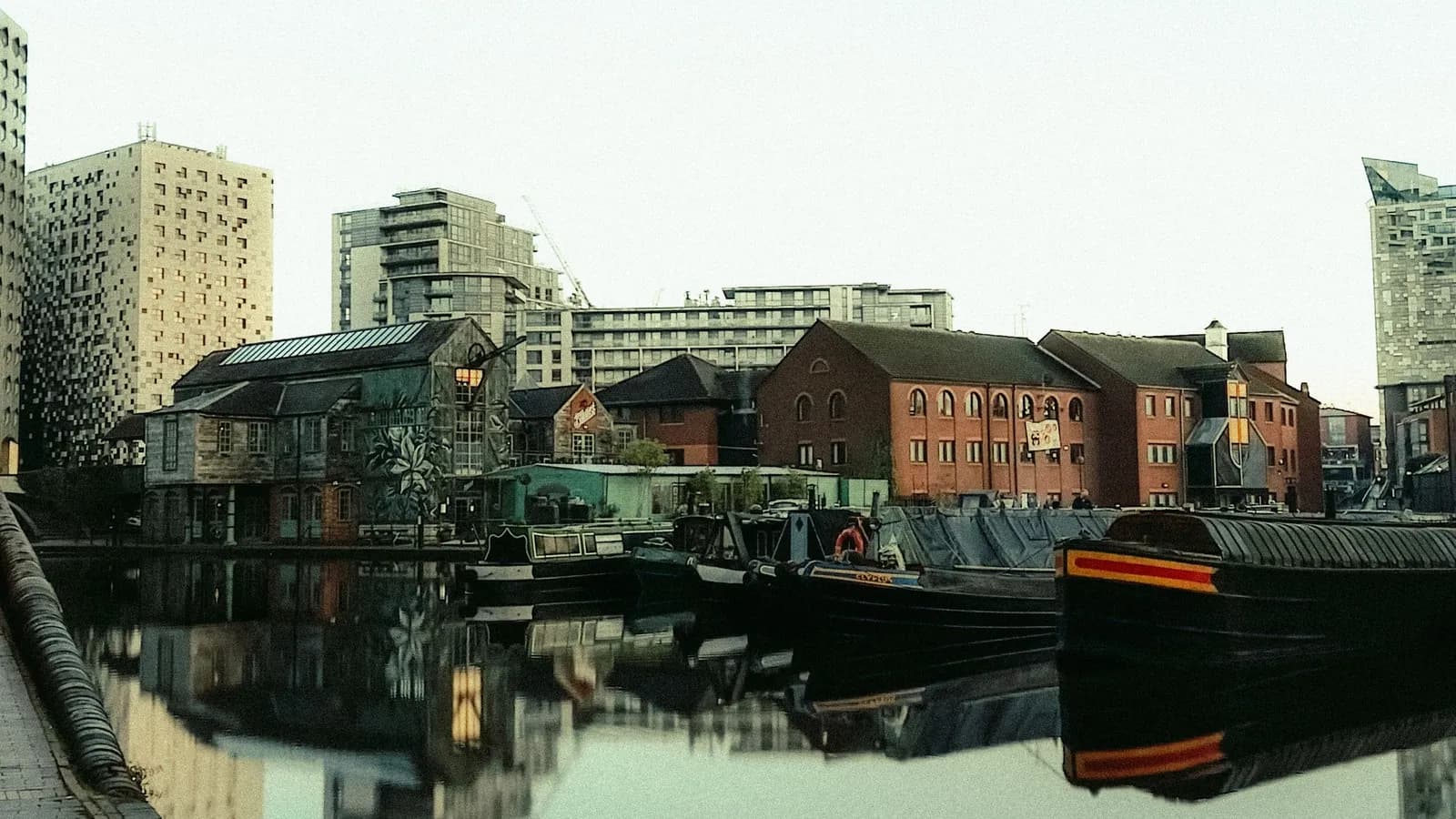 Narrowboats moored on a Birmingham canal in front of red-brick warehouses and modern apartment blocks
