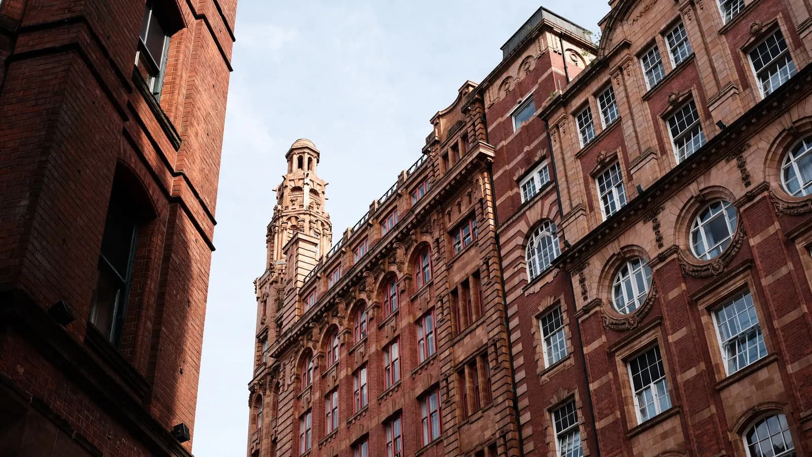 Looking up at red brick and terracotta Edwardian commercial buildings with a turret in central Manchester