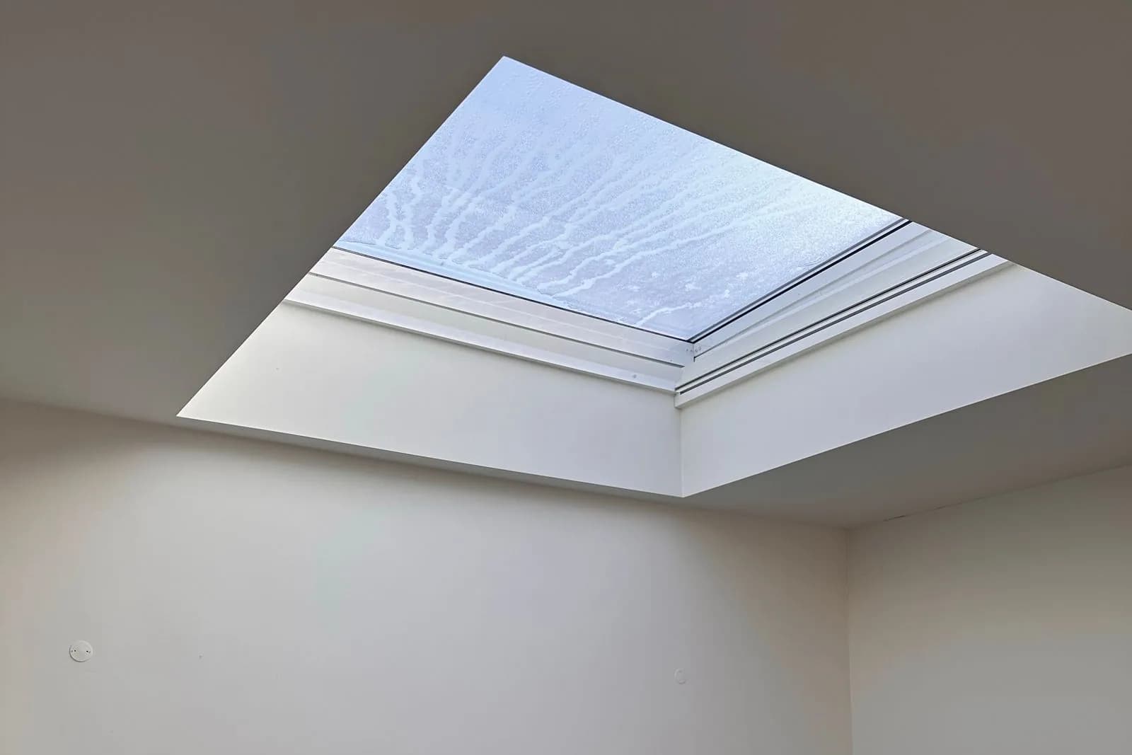 Large rooflight set into the ceiling of a pale, plain room