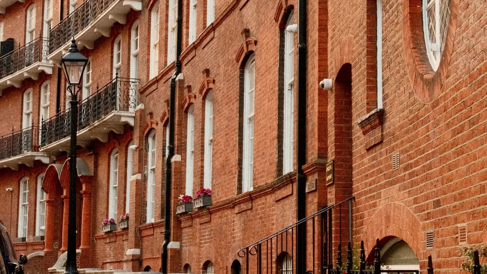 A terrace of red brick Victorian houses with wrought-iron balconies and a street lamp in London