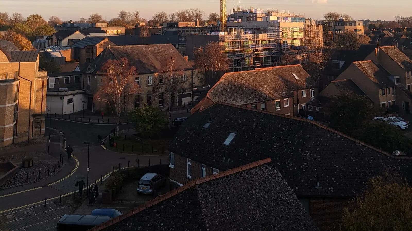 Slate and tiled roofs of an Oxfordshire town at sunset with a scaffolded new building and crane behind