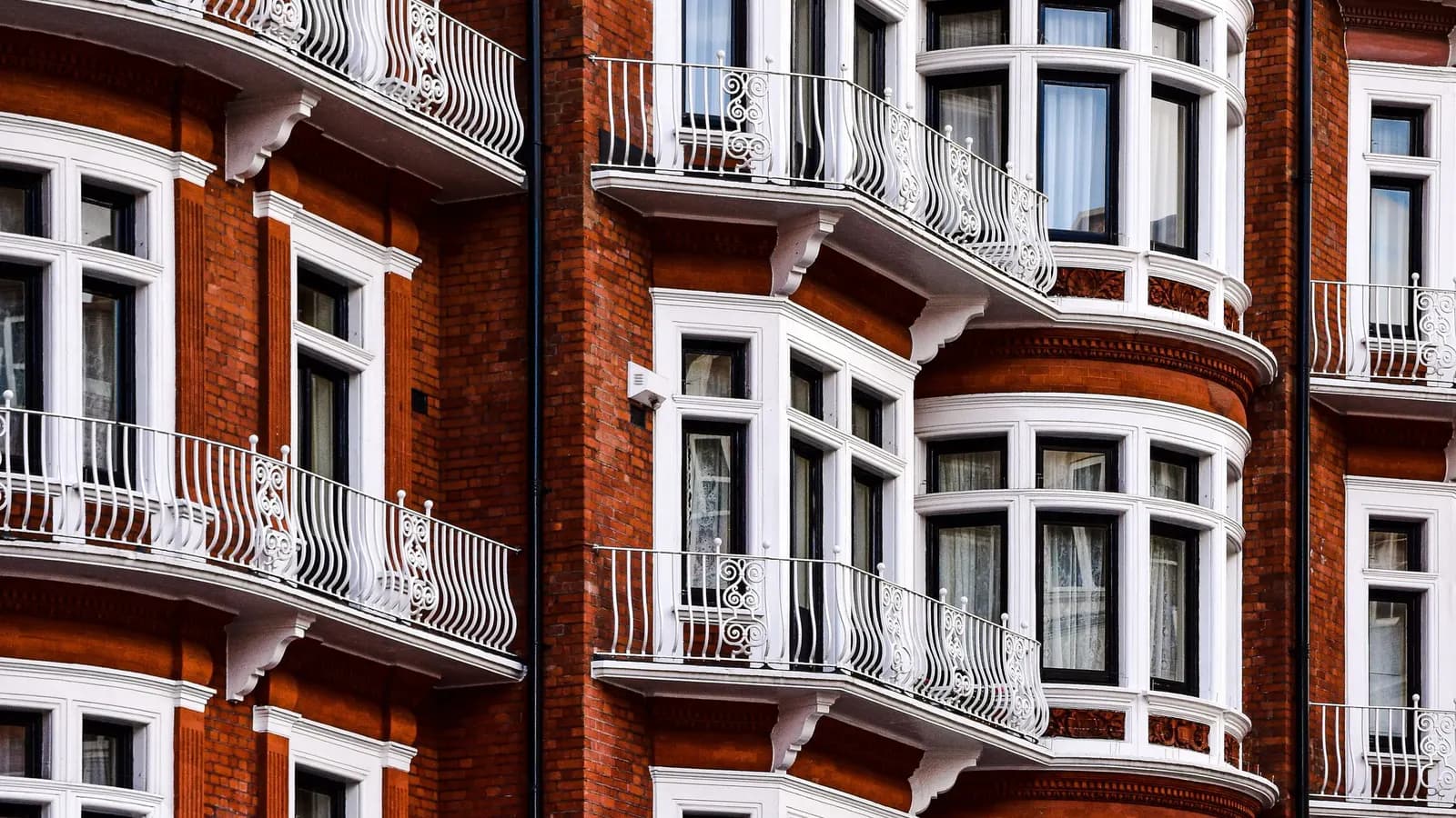 Red-brick Victorian building in London with white bay windows and ornate wrought-iron balconies
