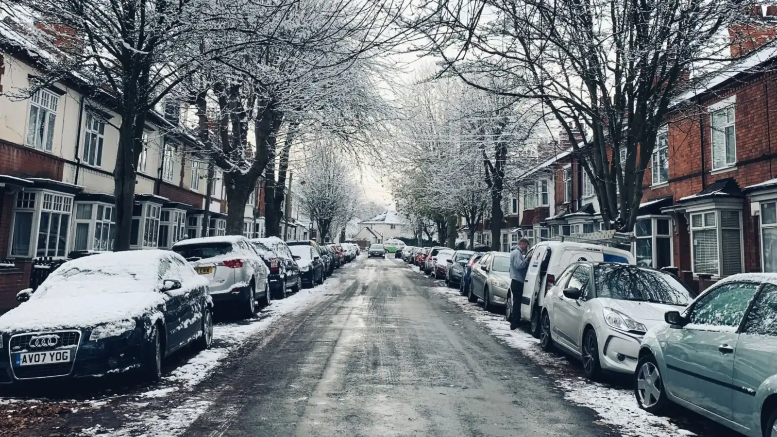 A snow-dusted Leicester street lined with parked cars and bare trees, with red-brick Edwardian terraces and bay windows on both sides