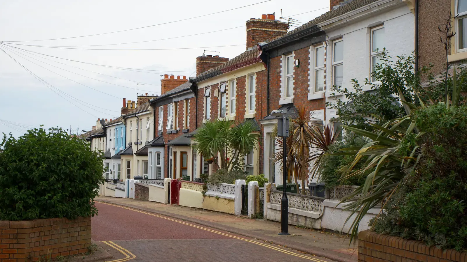 A Liverpool street of Victorian red brick and rendered terraced houses with chimneys, low front walls and palm-like garden plants under an overcast sky