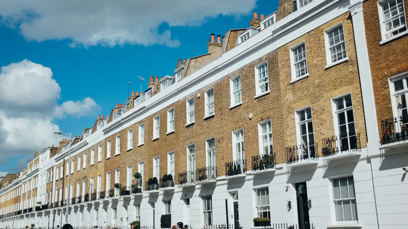 A long curving terrace of yellow-brick and white stucco townhouses in London, with dormer windows and chimney pots under a blue sky