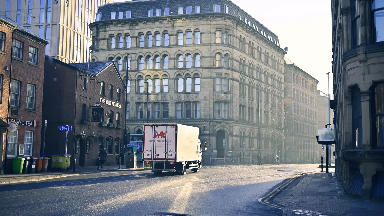 Early morning light on a Manchester street with a stone Victorian warehouse building, a brick pub and a delivery lorry